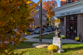 A small monument with yellow flowers stands in front of a brick courthouse building labeled "Cherokee County Courthouse" on a sunny autumn day.