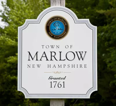 White sign for the Town of Marlow, New Hampshire, indicating it was granted in 1761, with a town seal at the top and trees in the background.